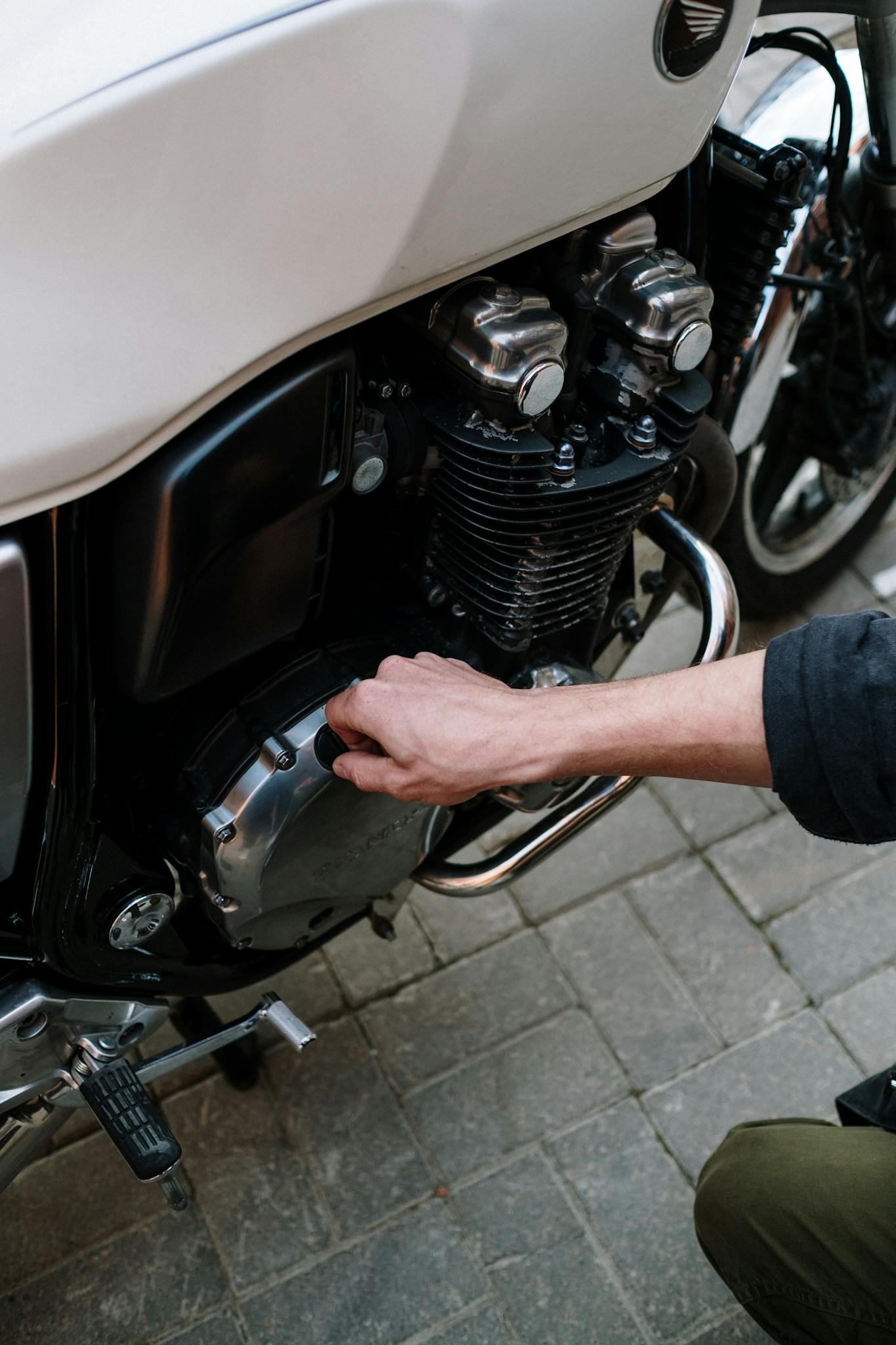 Close-up of a person working on a motorcycle engine outdoors.